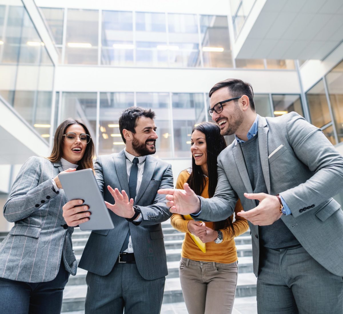 Group of dedicated businesspeople standing in front of business center and talking about job. One of them holding tablet and pointing at it.